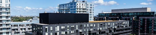 A large black building with many windows is surrounded by other buildings and a parking lot.