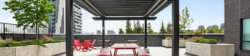 A patio with a pergola and red chairs.