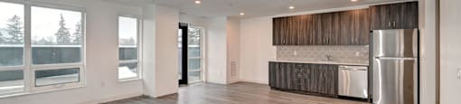 A spacious room with wooden flooring and a kitchen area in the background.