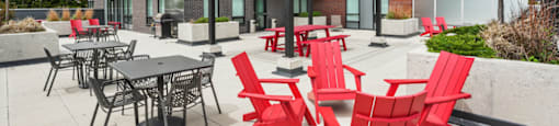 A patio with red chairs and tables is in front of a brick building.