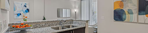 A modern kitchen with a granite countertop and a bowl of fruit on it.