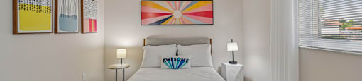 A bedroom with a bed, two lamps, and a painting on the wall.