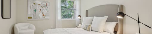 A bedroom with a bed, chair, and lamp.