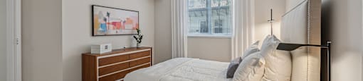 A bedroom with a large bed, a nightstand, and a window with curtains.
