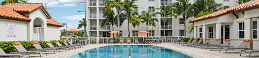 A large swimming pool in front of a hotel with a white building and palm trees.