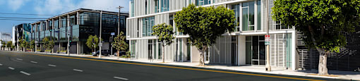 A modern building with a glass facade is situated on a street with a clear blue sky above.
