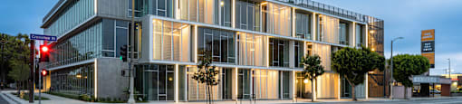A modern building with a glass facade is illuminated from within and surrounded by a yellow crosswalk.