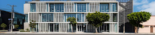 A modern building with a glass facade and trees in front.