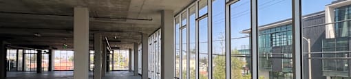 A large empty room with concrete pillars and windows overlooking a street.