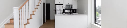 A white interior with a staircase and a kitchen area.