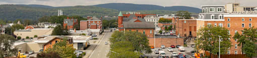 A parking lot with cars and a road in the foreground with buildings and trees in the background.