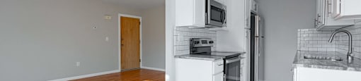 A kitchen with white cabinets and appliances, a wooden floor, and a door to another room.