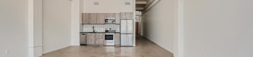 A large empty room with a kitchenette in the background.