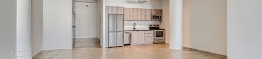 A kitchen area with a sink, stove, and refrigerator in a room with a concrete floor and white walls.