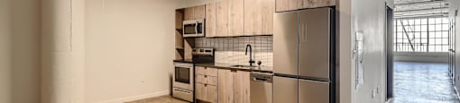 A kitchen with a sink, stove, and refrigerator in a large empty room.