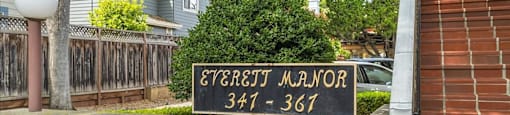 A sign for the Evergift Manor apartment complex is displayed in front of a brick wall.