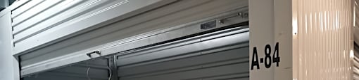 A closed grey shutter with a white handle and a white door with A-84 on it.