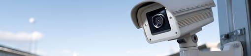 A security camera is mounted on a pole overlooking a road.