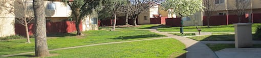 Large lawn with trees and concrete walkway with red fencing at American River Gardens, Sacramento
