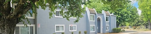 A multifamily housing building with a tree in the foreground.