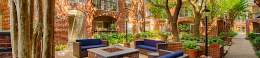A courtyard with a fire pit and chairs surrounded by trees at The Inverness Apartments in Houston, TX