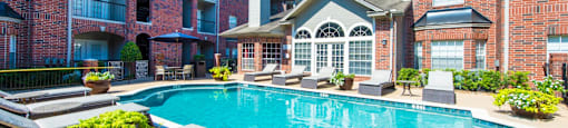 A swimming pool surrounded by lounge chairs and plants at The Inverness Apartments in Houston, TX