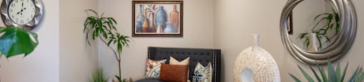 A living room with a couch, a rug, a plant, and a clock on the wall.