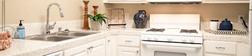 A white kitchen with a stove, sink, and cabinets.