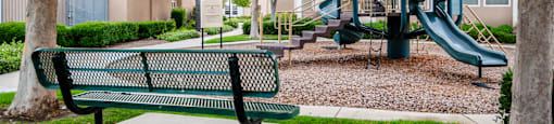 A green park bench sits in front of a playground.