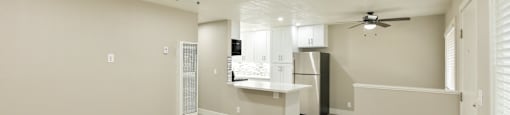A spacious room with a ceiling fan and a kitchen area in the background.