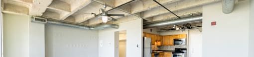 A spacious room with wooden flooring and a kitchen area in the background.