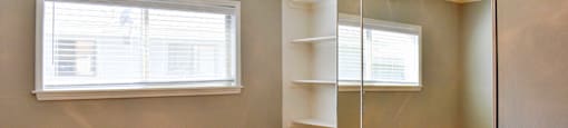 View of other side of bedroom with wood look flooring, floor to ceiling sliding glass mirror closet with built in shelving, and ceiling fan