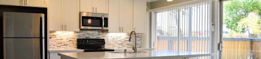 View of kitchen with island. Featuring wood look flooring, white countertops, white cabinets, stainless appliances, and tile backsplash.  Access into private patio/balcony through sliding glass door