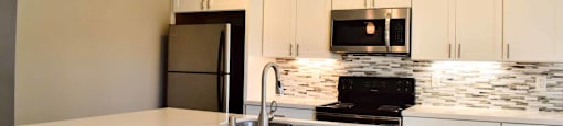 kitchen with island, all white countertops, white cabinets, stainless appliances, and tile backsplash
