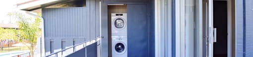 private balcony with sliding glass door open into home, and stacked washer and dryer in outside utility closet