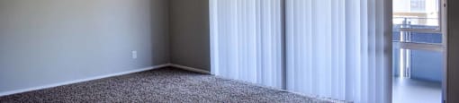 Carpeted bedroom view into private patio/balcony through sliding glass door with vertical blinds