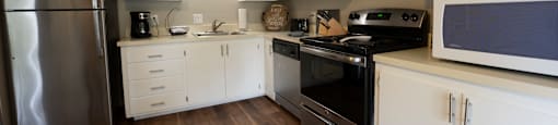 view of furnished model kitchen, with stainless appliances, wood look flooring, white cabinets, and well decorated