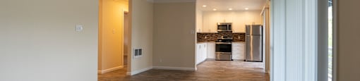 a living room with a ceiling fan and a kitchen in the background