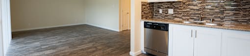 View from kitchen into living room, shows stone counters, tile backsplash, stainless appliances, white cabinets, wood look flooring and ceiling fan