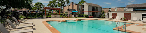 Gated community pool with lounge chairs, seating under umbrellas, and grilling station under pergola