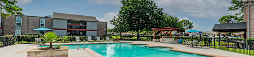Gated community pool with lounge chairs, seating under umbrellas, and grilling station under pergola