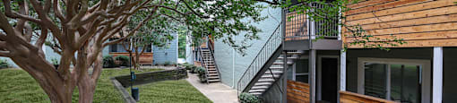 Exterior view of building with sidewalk winding through lush grass and trees