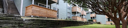 a grassy area with a tree in front of an apartment building
