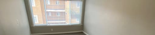 View of room with wood look flooring, ceiling fan, and well lit almost floor to ceiling window.