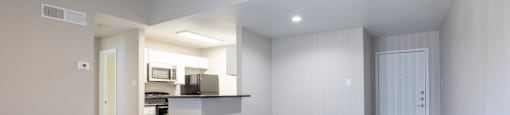 an empty living room with a kitchen in the background