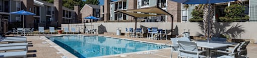 A pool area with chairs and umbrellas in front of a building.