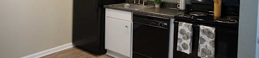 View of kitchen with dark counters, black appliances, and white cabinets with wood look flooring