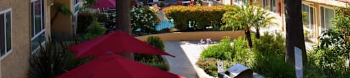 Elevated view of courtyard with grilling station and picnic tables with umbrellas for seating with lush landscaping