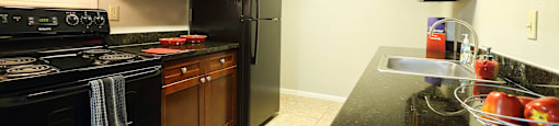 kitchen area with tile flooring, dark counters, black appliances, and brown cabinets