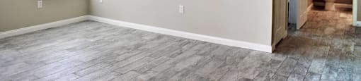 View from living room with well lit window and ceiling fan towards hall with bathroom, has wood look flooring